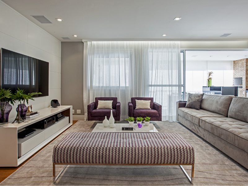 Sala de estar com poltronas, cortinas brancas,, sofá cinza e televisão