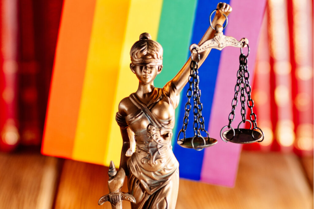 Estátua dama da justiça com bandeira LGBTQIA+ ao fundo