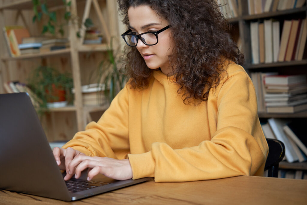 Menina de blusa amarela e cabelo cacheado sentada mexendo em um notebook