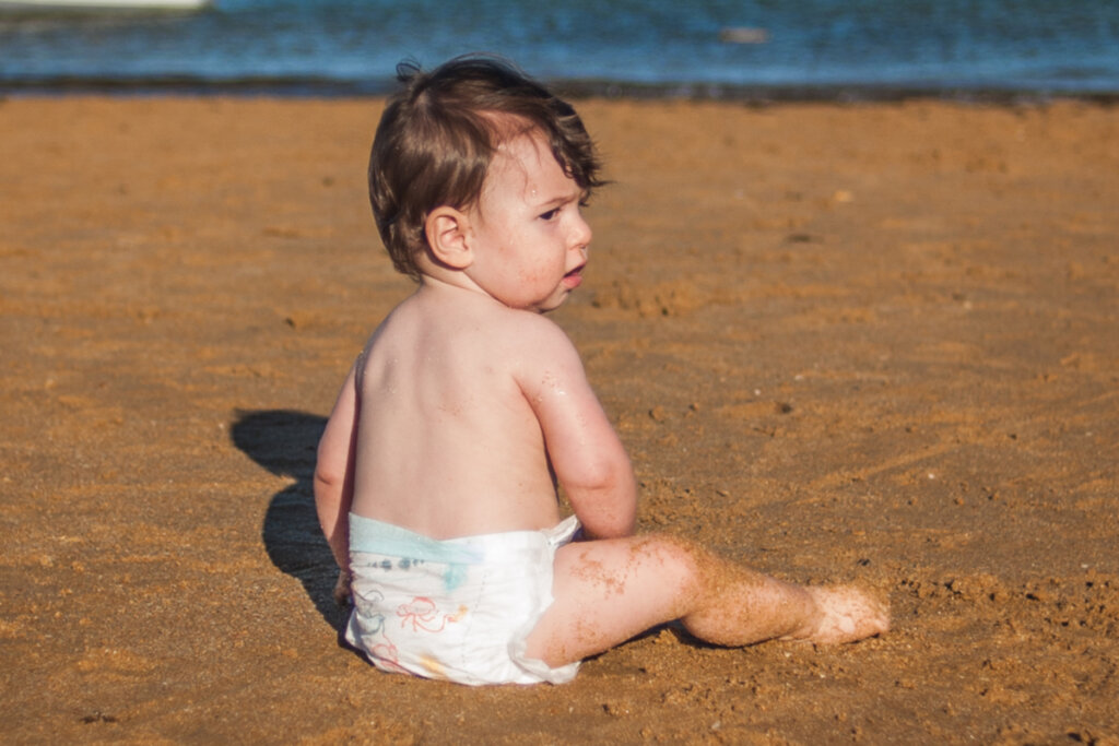 Bebê de fralda sentado na areia da praia