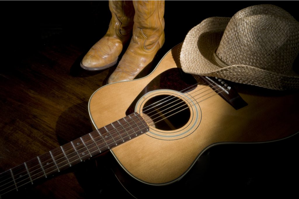 Um violão com um chapéu em cima dele e botas ao lado
