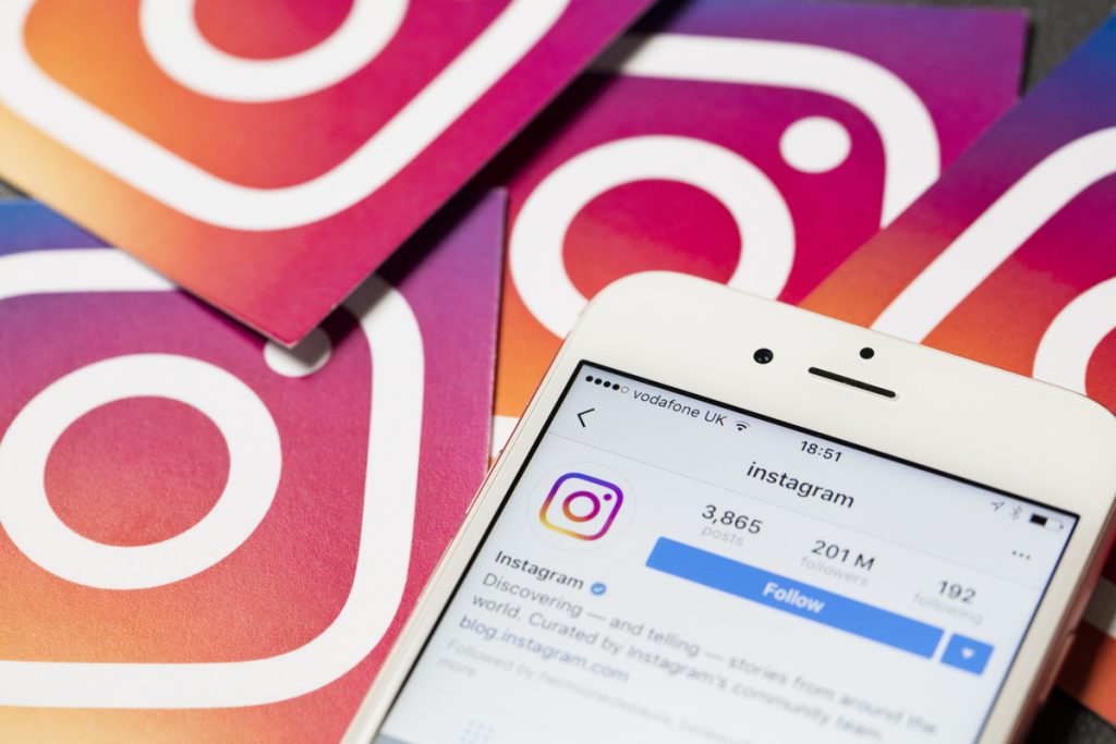 Celular com o feed do instagram aberto e logo da rede social em volta