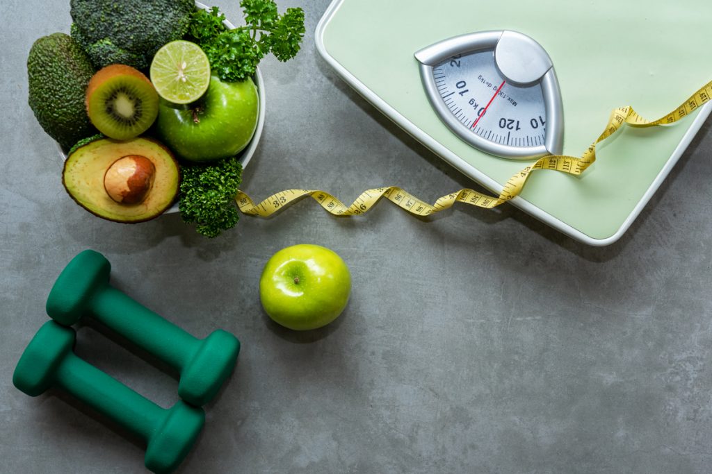Uma balança, uma fita métrica, pesos de academia e frutas verdes