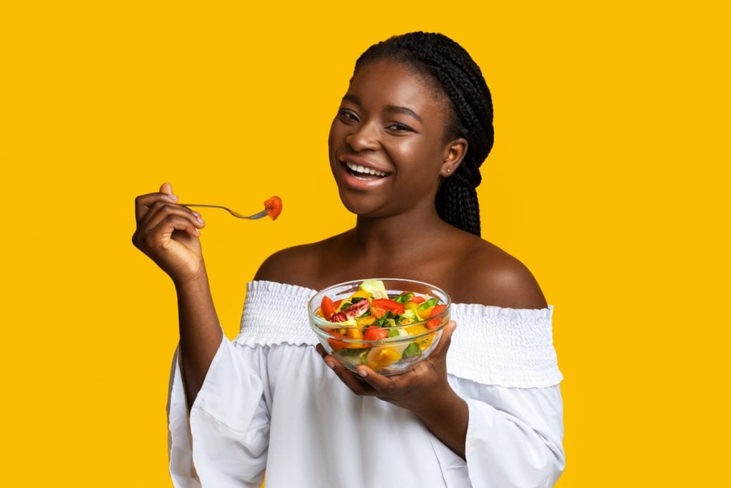 Mulher com blusa branca segundo um recipiente com salada e sorrindo