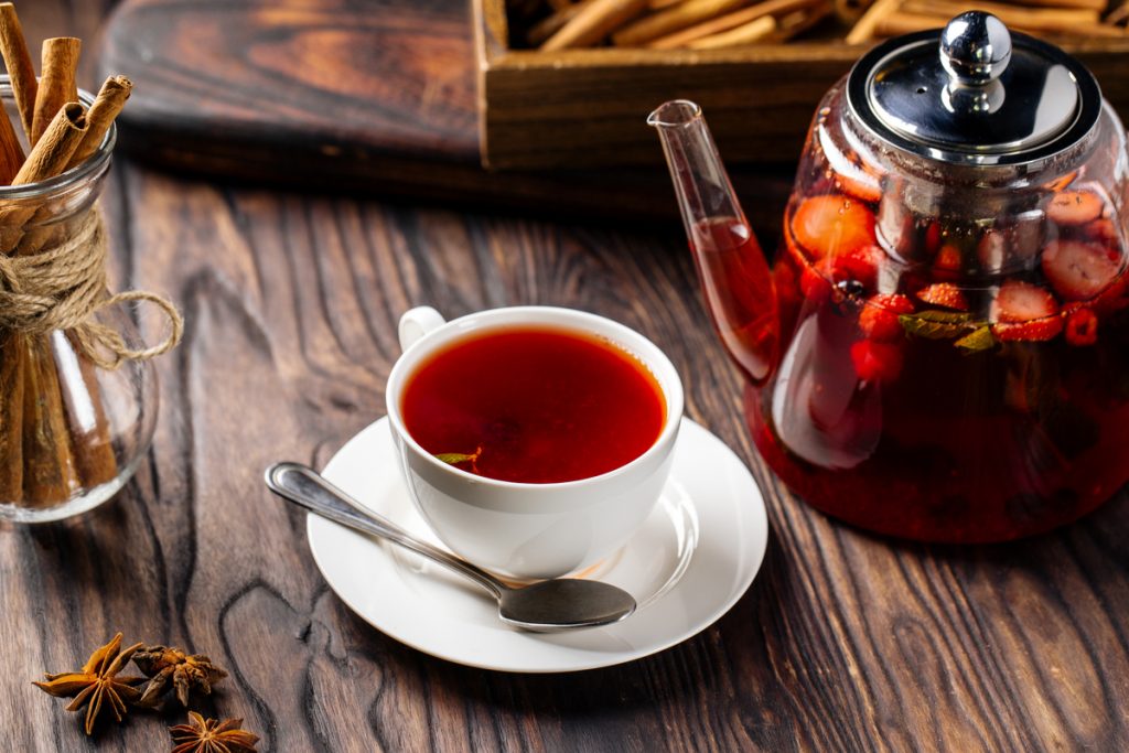 Xícara branca com chá vermelho. Bule de vidro com chá vermelho com frutas