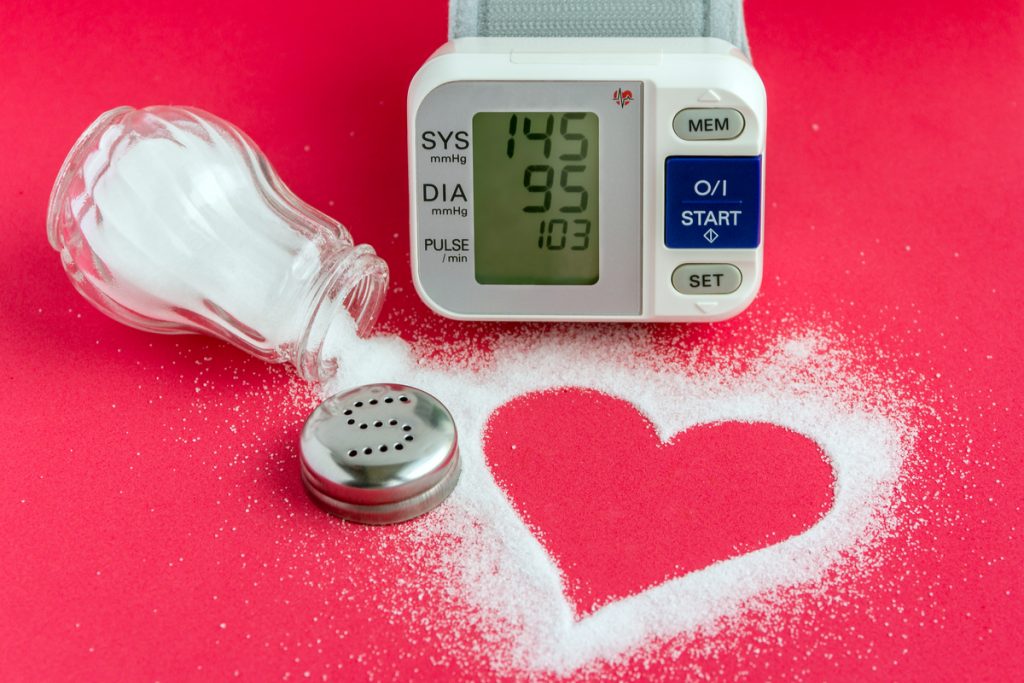 Um medidor de pressão arterial e um saleiro aberto derramando sal, que forma um coração