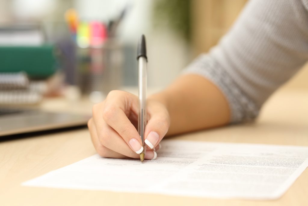Mão feminina segurando uma caneta e escrevendo em um papel