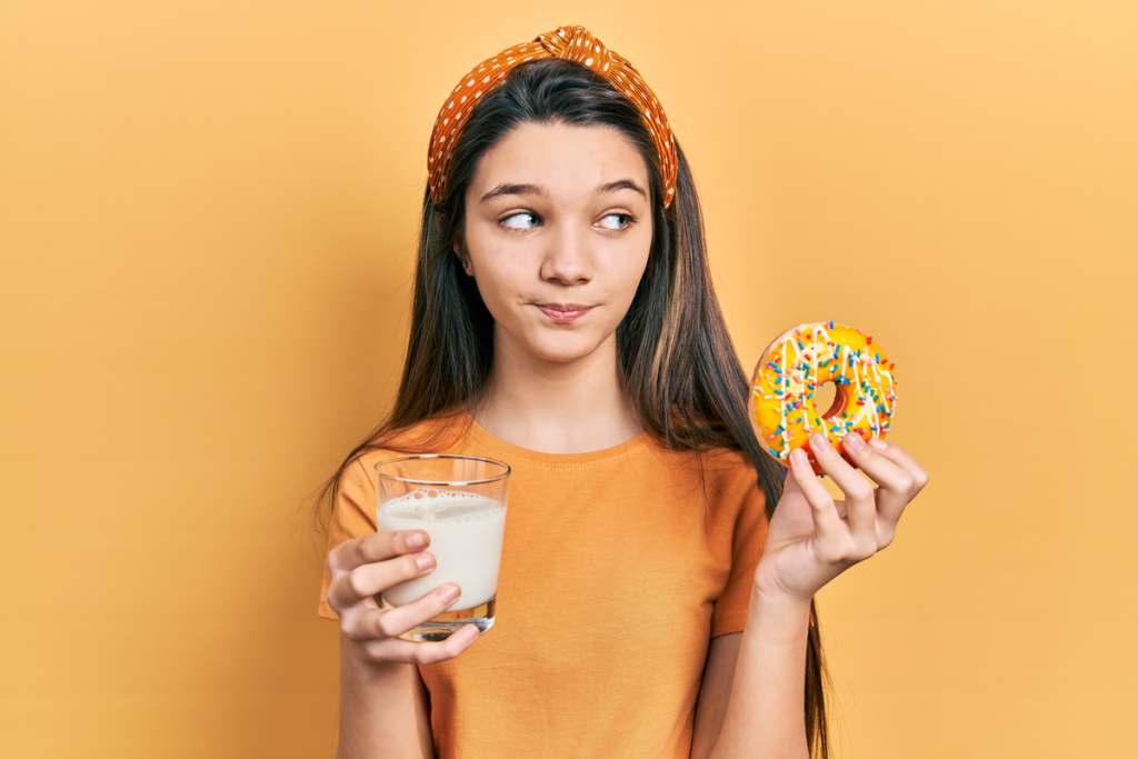 Menina segurando um donut em uma mão e na outra um copo com leite