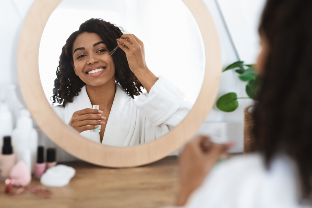 Mulher sorrindo passando produto na pele em frente a um espelho
