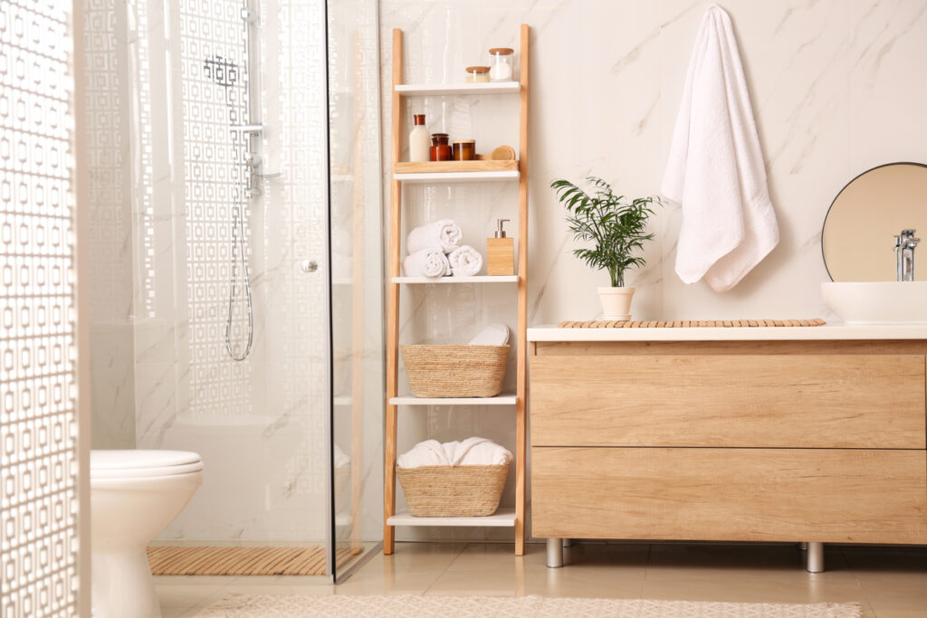 Banheiro branco com móveis marrom claro, toalha pendurada na parede e vaso de planta como decoração