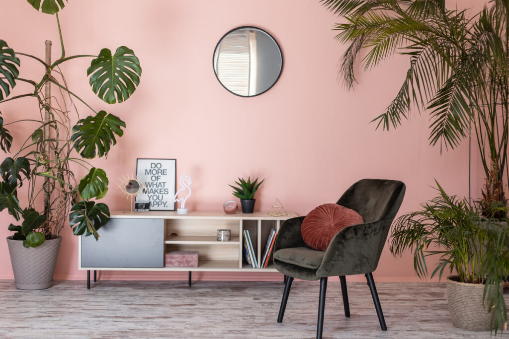 Sala de estar com parede rosa, cadeira marrom, espelho e plantas