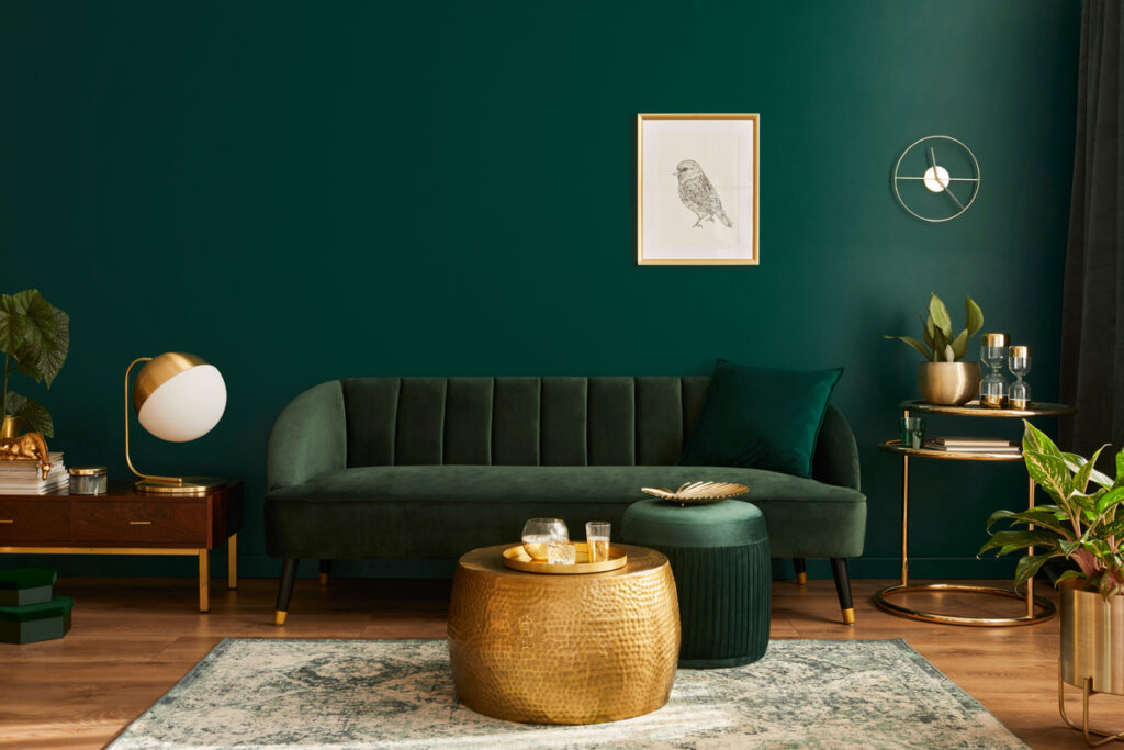 Sala de estar com parede verde escuro, sofá verde, tapete branco, mesa de centro e quatro branco pendurado na parede