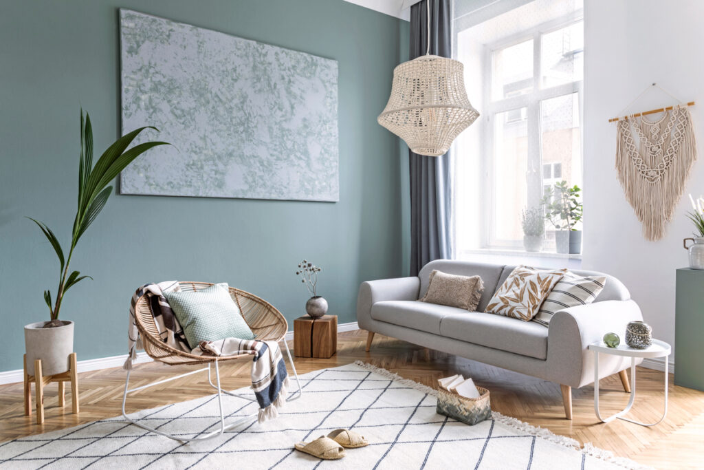 Sala de estar com parede verde, sofá, quadro branco e vaso de planta 