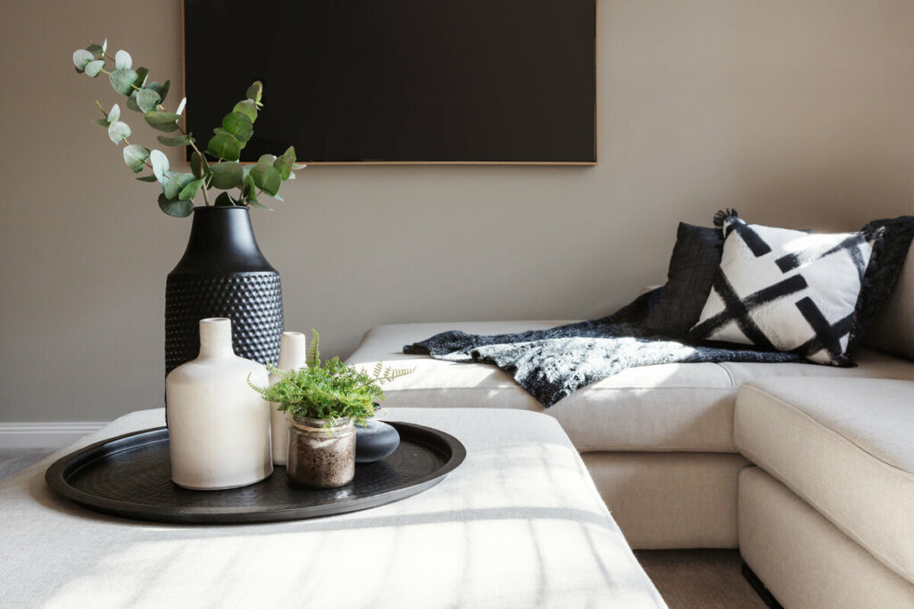 Mesa branca com vasos de planta preto e sofá bege ao fundo 