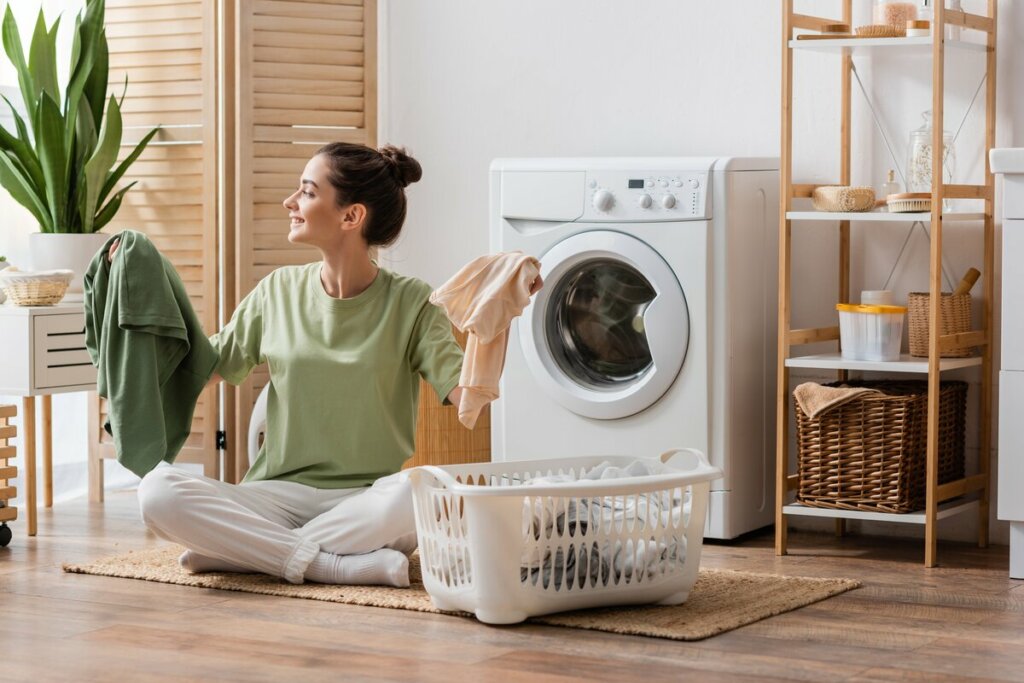 Mulher de blusa verde sentada sorrindo separando roupas para lavar 