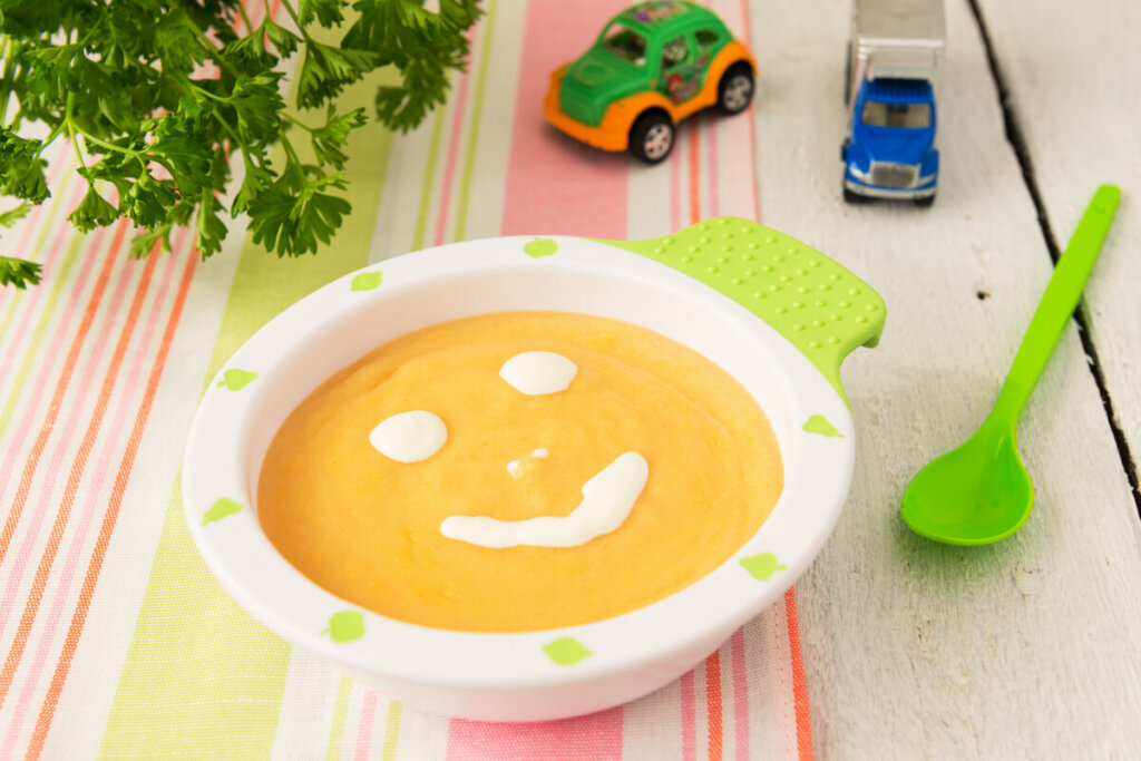 Prato de criança branco e verde com sopa decorado com um sorriso