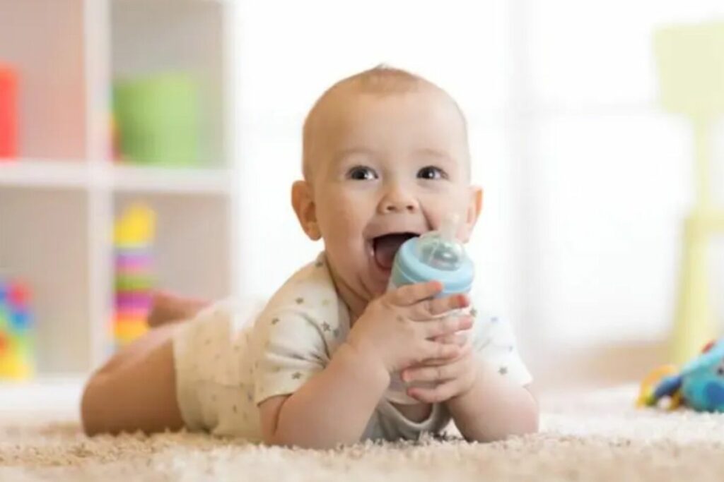 Bebê sorrindo segurando uma mamadeira deitado em um tapete