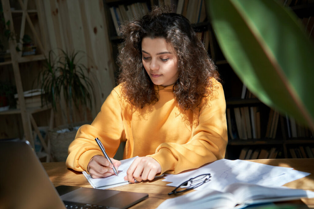 Menina de blusa amarela sentada escrevendo em um papel