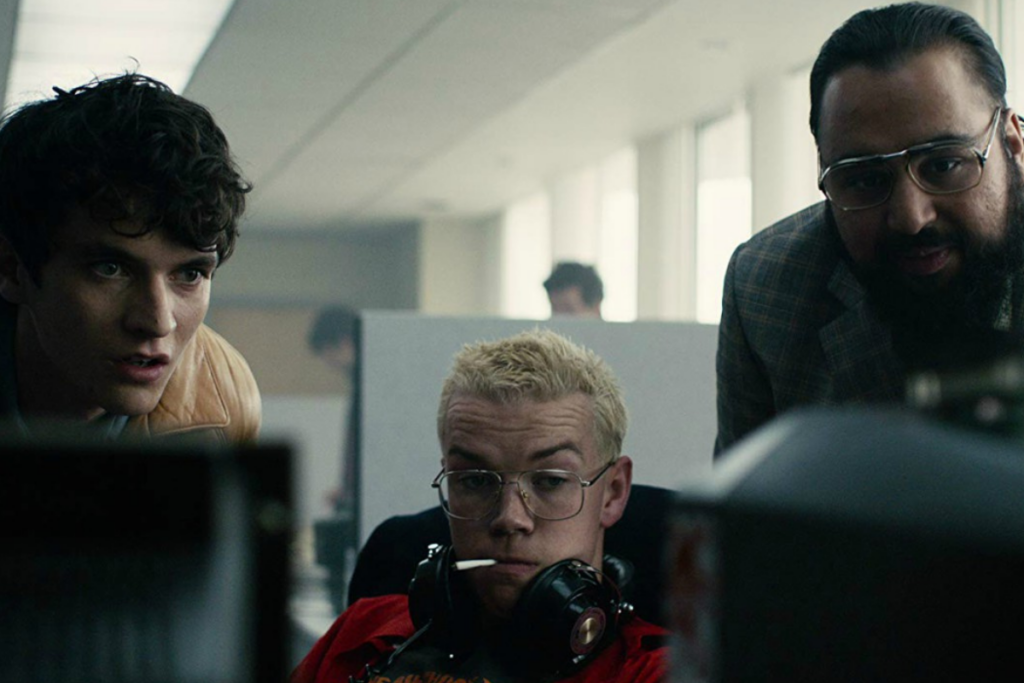 Cena do filme "Black Mirror: Bandersnatch". Três homens olhando para tela de computador
