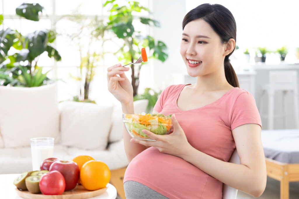 Mulher grávida sorrindo e se alimentando com frutas