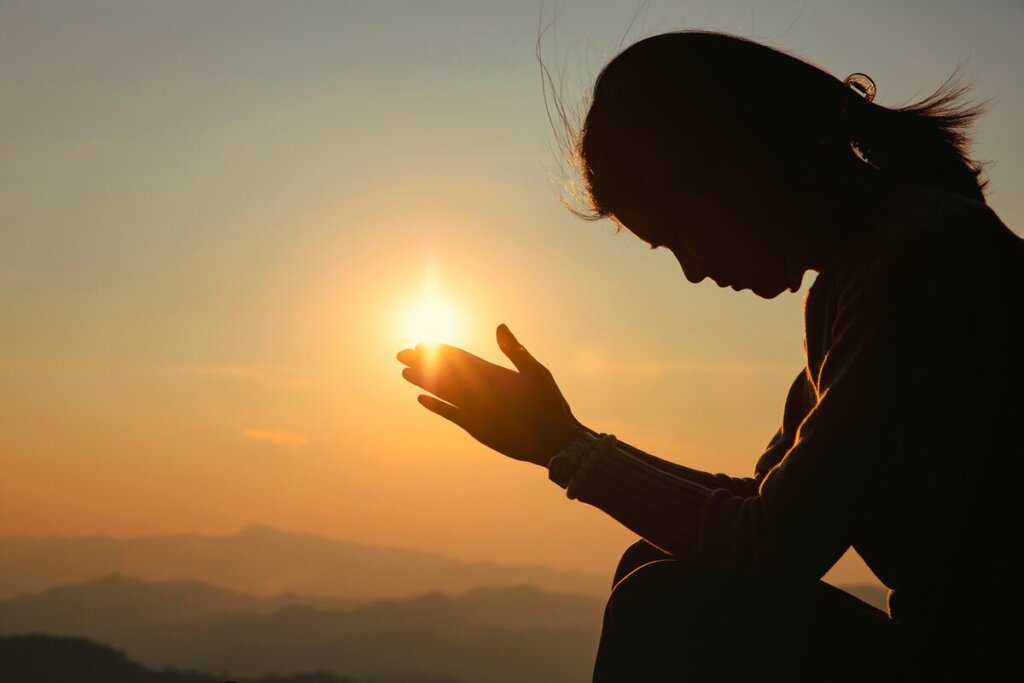 Mulher sentada orando em um por do sol 