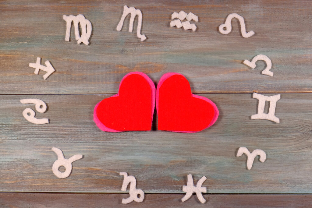 Dois corações em cima de uma mesa de madeira rodeado com os doze signos do zodíaco