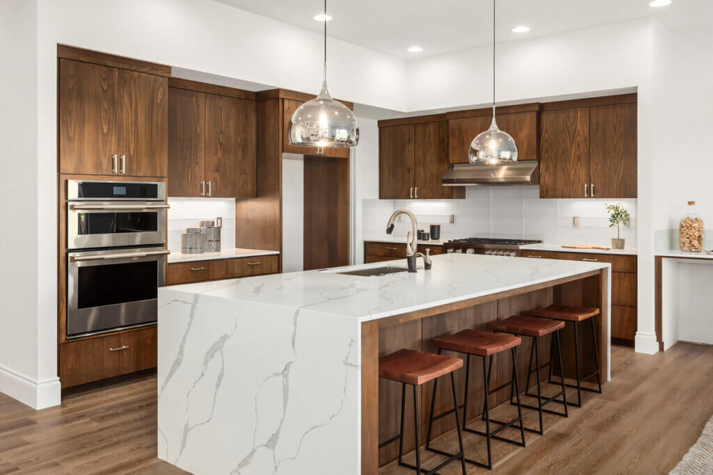 Imagem de uma cozinha luxuosa, com bancadas em mármore e tons amadeirados nos armários planejados