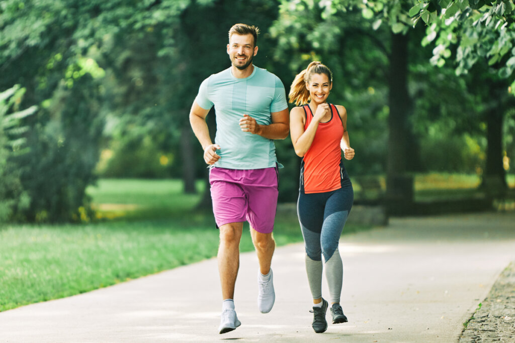 Homem e mulher correndo em parque com semblantes alegres.