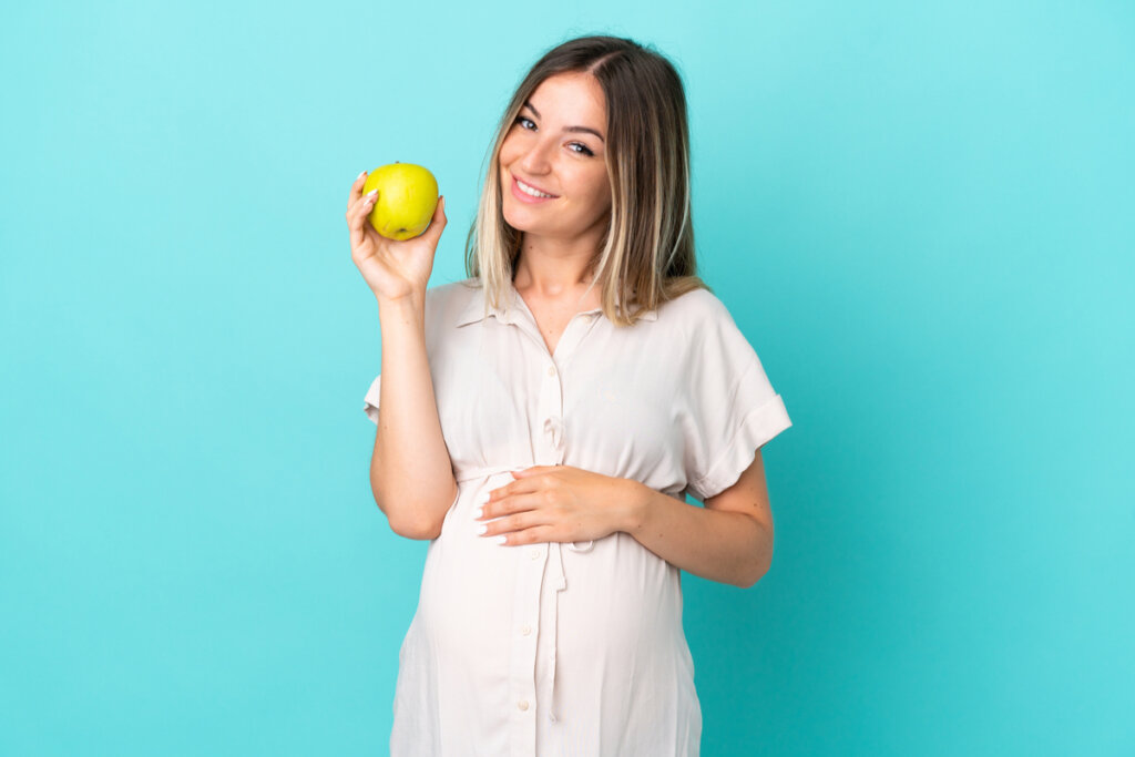 Mulher grávida de vestido branco segurando uma maçã