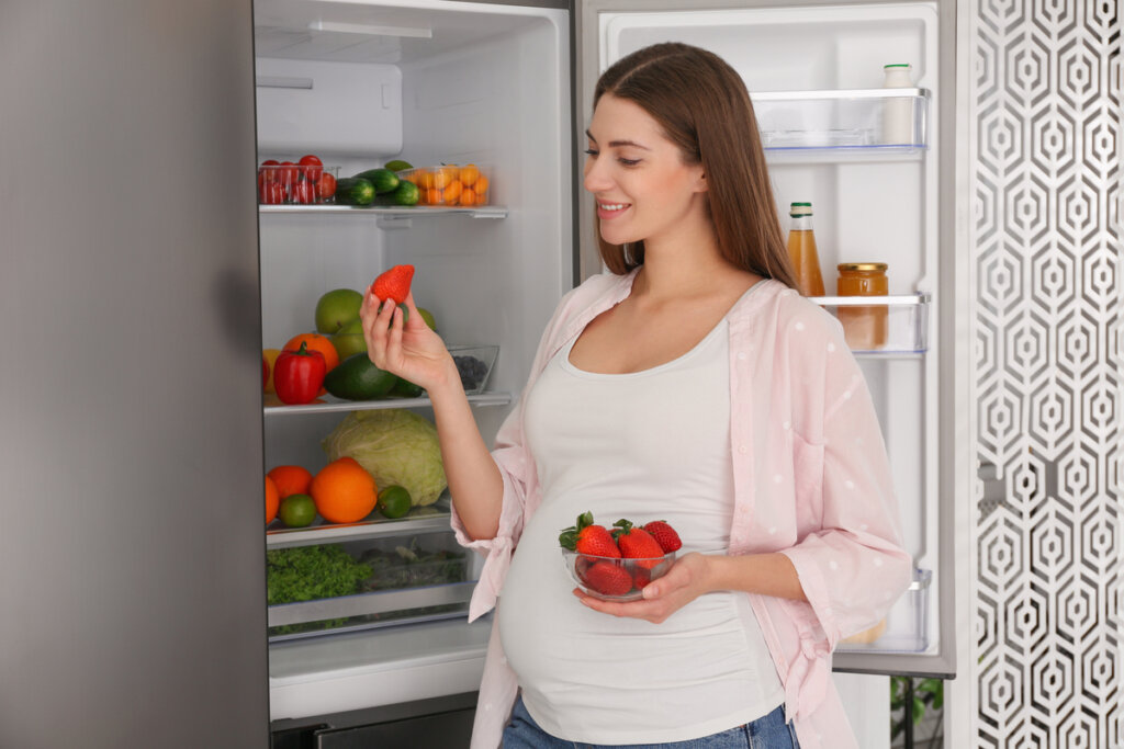 Gestante mexendo em alimentos em frente à geladeira