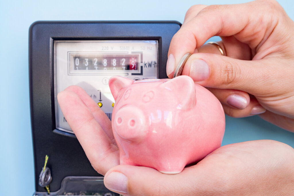 Mãos femininas seguram moeda e cofrinho de porco em um fundo de um medidor de eletricidade
