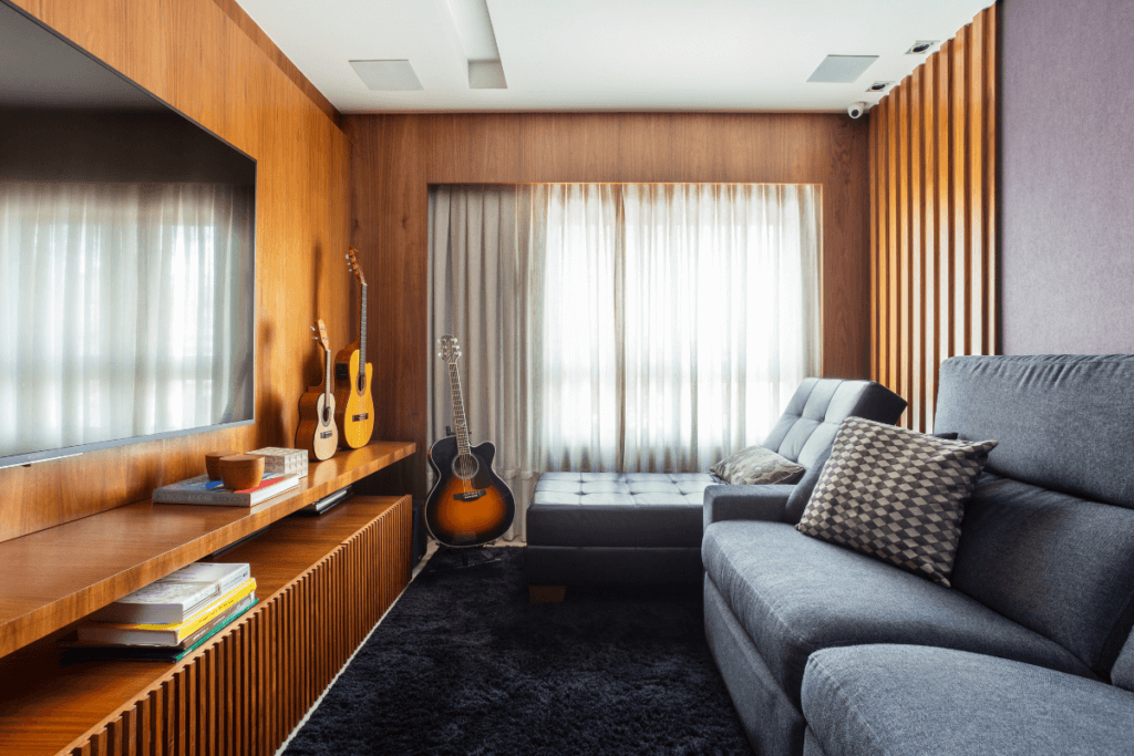 Sala de estar com cortina branca, sofá cinza e televisão