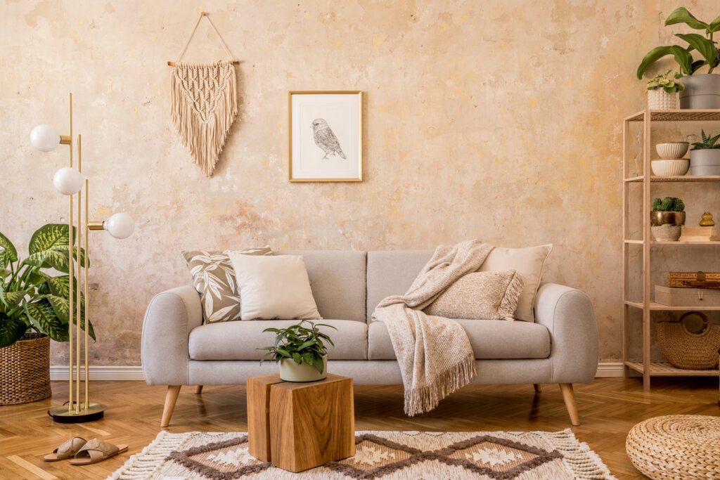 Sala de estar com sofá cinza, parede bege, tapete, plantas e quadro 