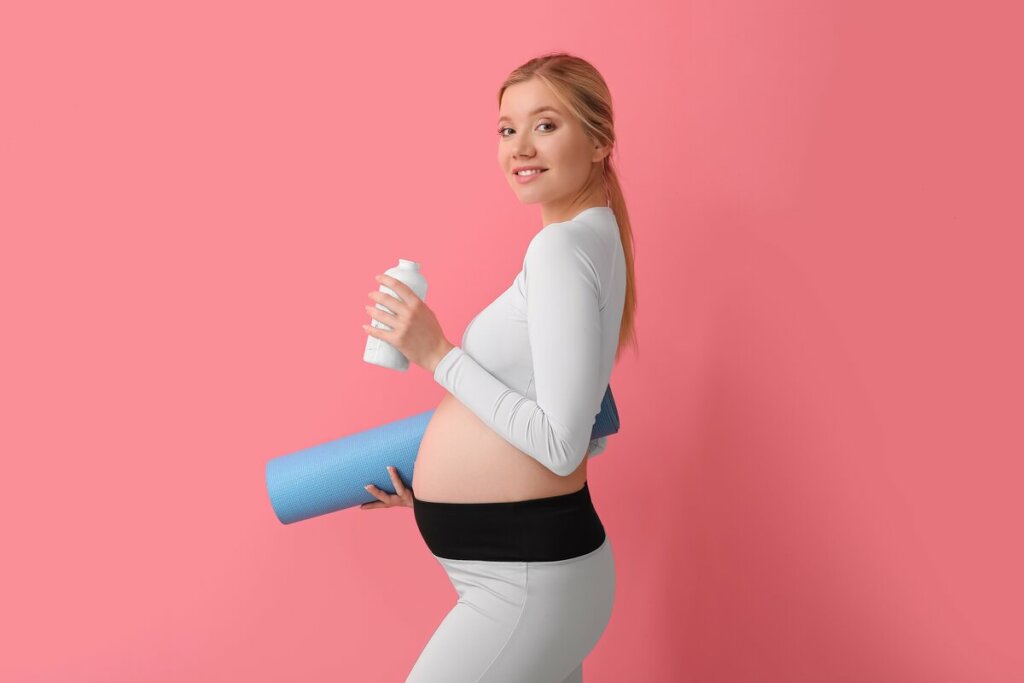 Mulher grávida sorrindo segurando garrafa e tapete