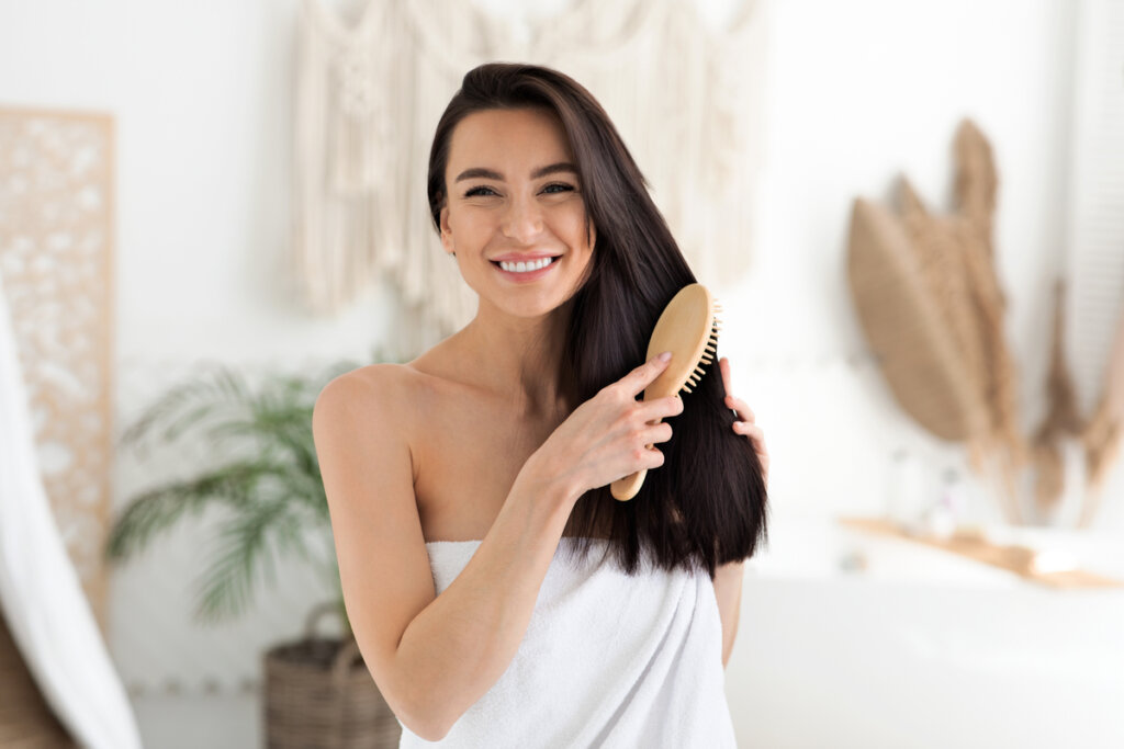 Mulher com toalha branca sorrindo e penteando os cabelos