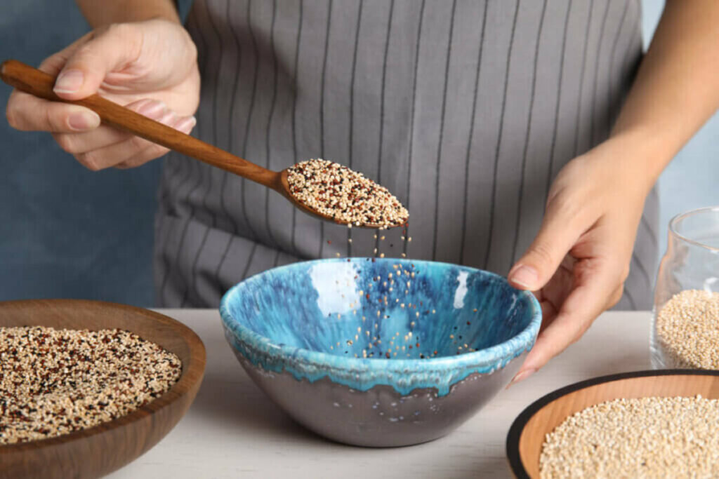 Mãos feminina colocando sementes de quinoa em um recipiente azul