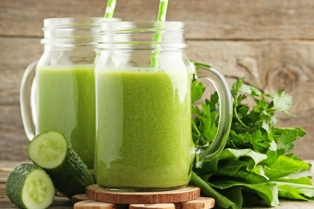 Suco verde em canecas de vidro com canudo e pepino e couve ao redor