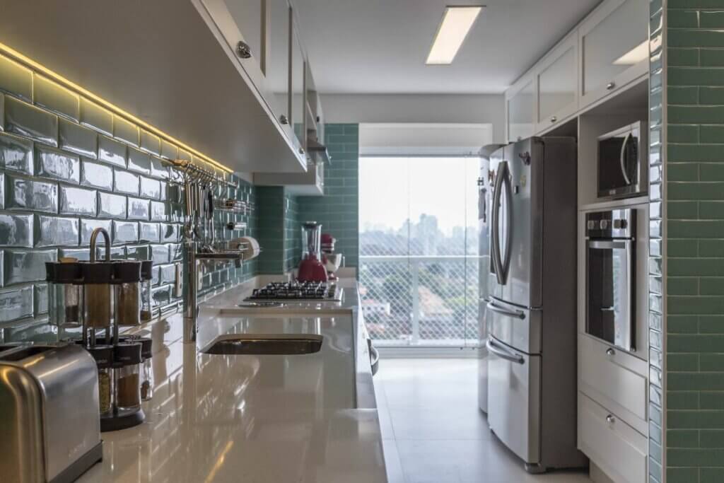 Vista da cozinha com bancada e utensílios em cima, geladeira e torre quente com gavetas