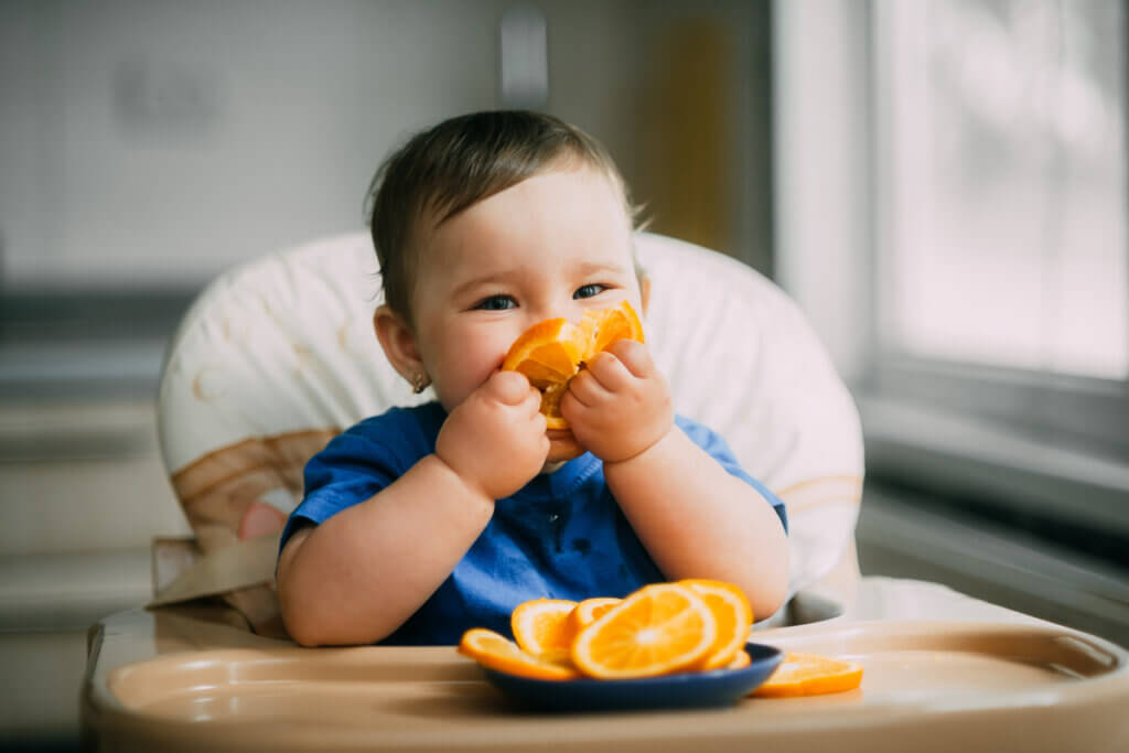 Bebê sentado em cadeira e comendo laranja