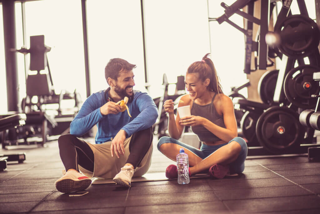 Homem e mulher em uma academia sentados comendo