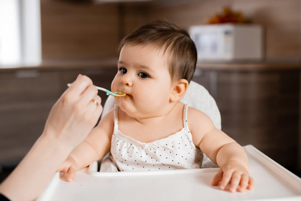 Bebê em cadeira branca sendo alimentado com uma colher