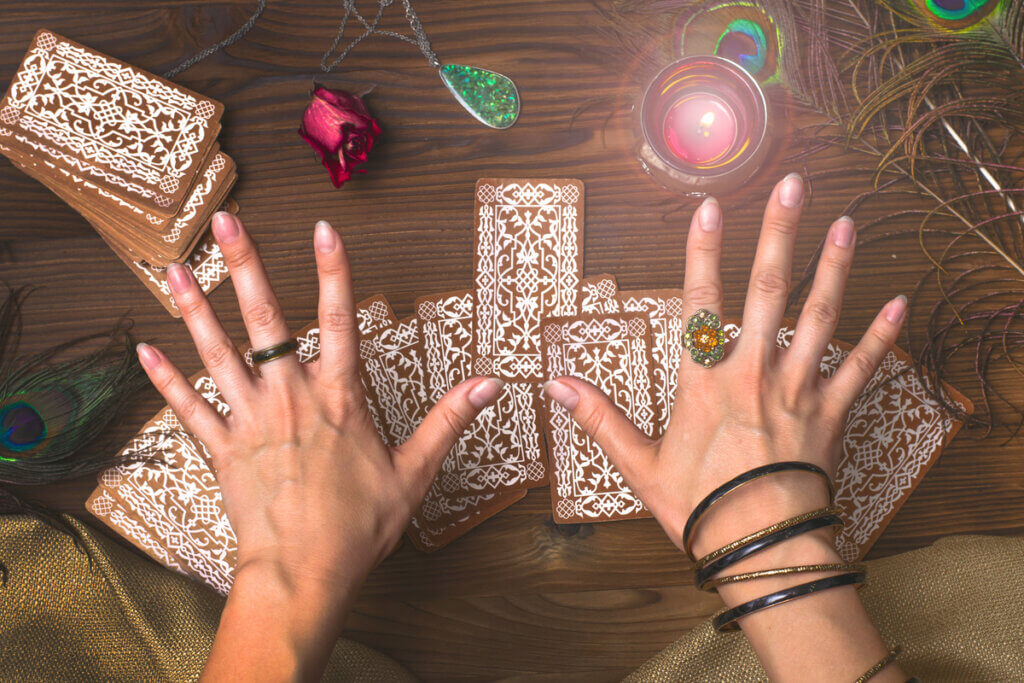 Mãos com anéis sobre cartas de tarô em mesa