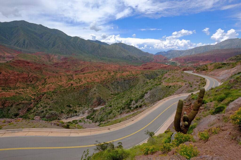 Estrada divide paisagem com montanhas vermelhas e com folhagens 
