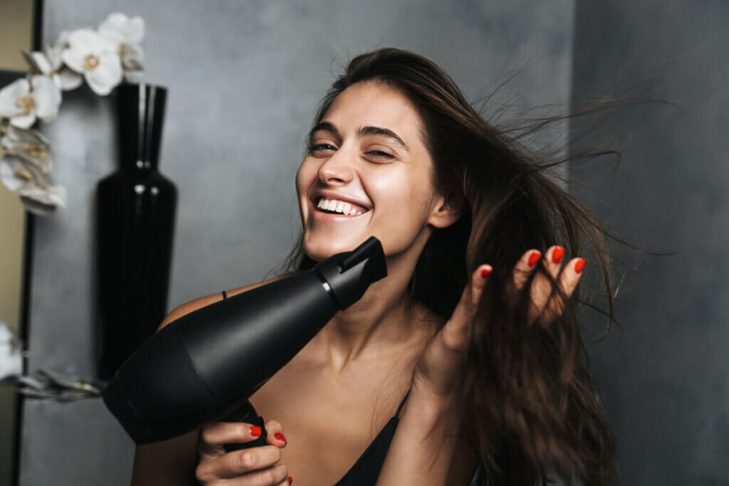 Mulher sorrindo secando o cabelo com secador