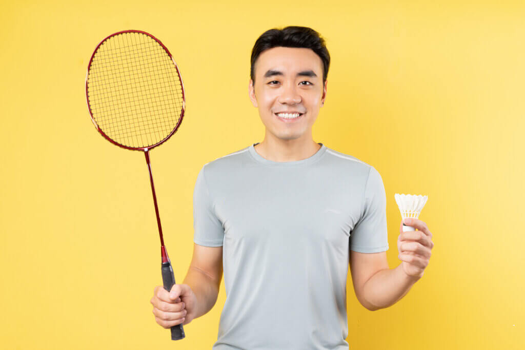Homem sorrindo segurando raquete e peteca
