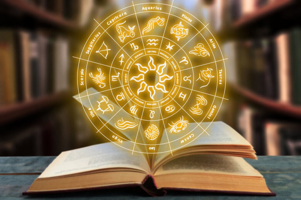 Livro aberto em cima da mesa com ilustração de um círculo com os 12 signos do zodíaco