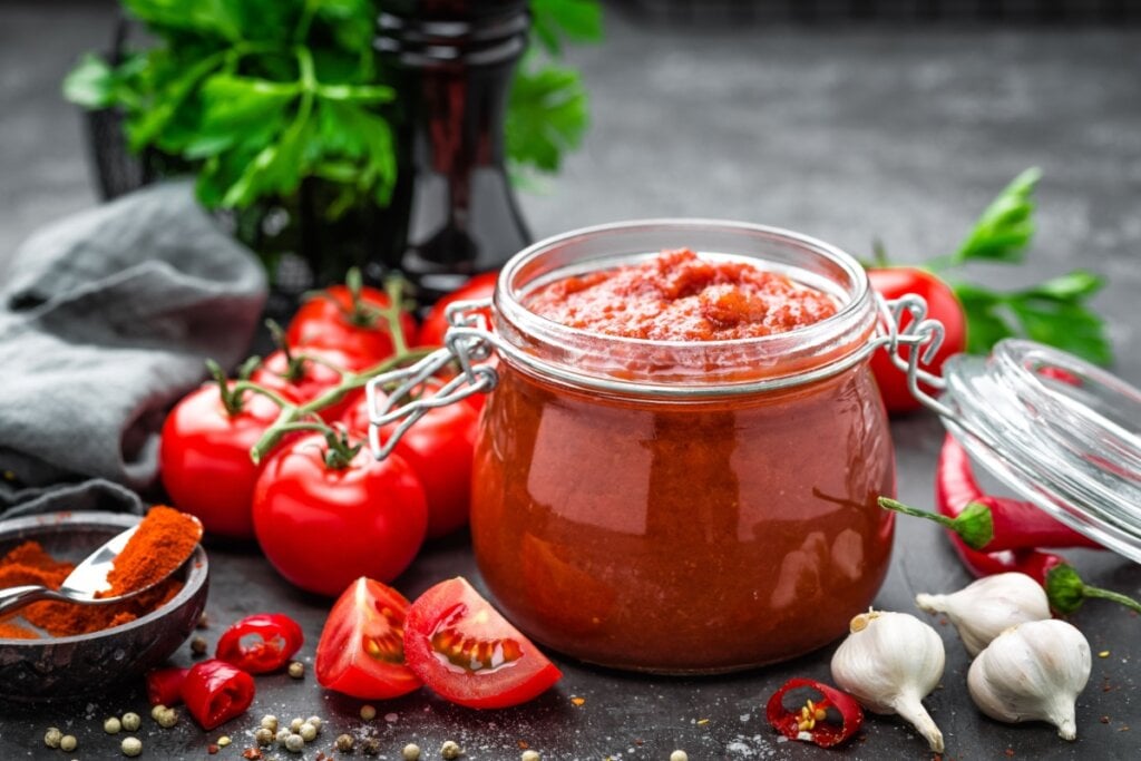 Molho de tomate em recipiente transparente com pedaços de tomate, pimenta e alho em volta