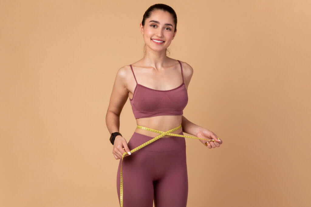 Mulher com roupa de academia medindo a cintura com uma fita