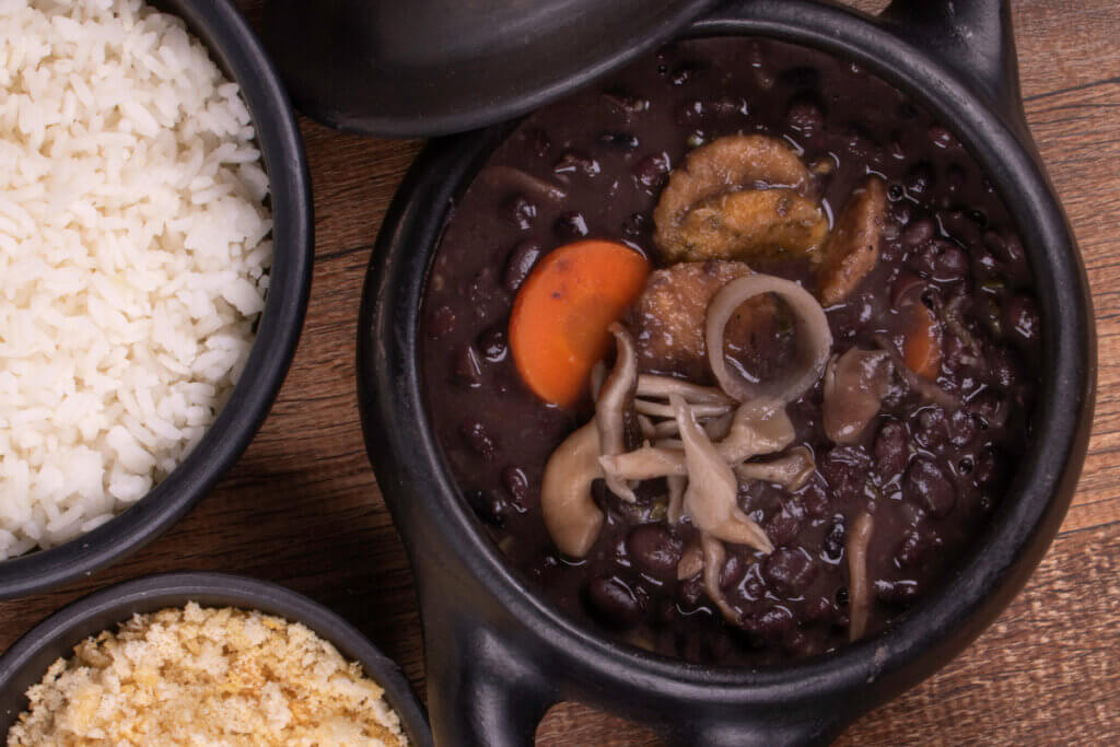 Feijoada vegana no bowl preto e bowl com arroz e farofa ao lado