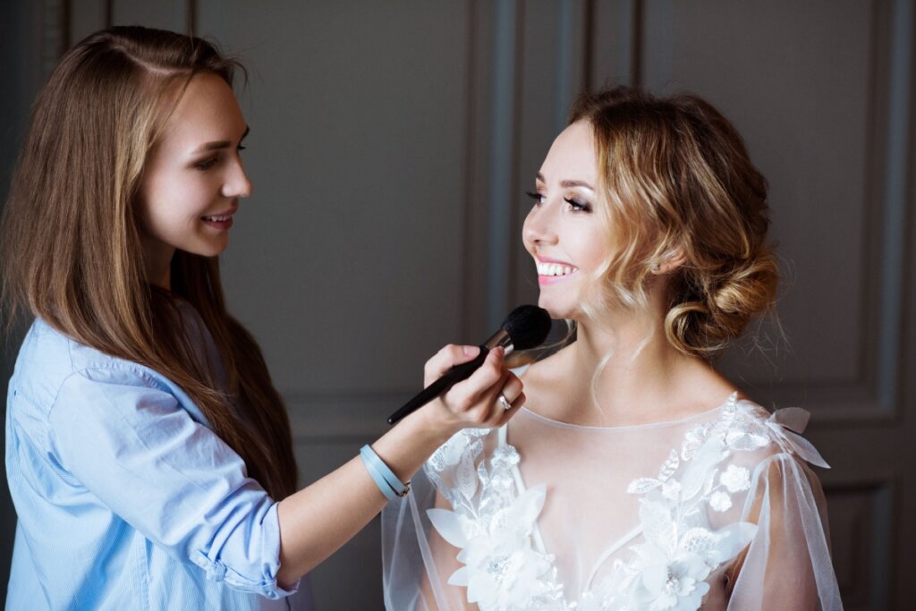 Maquiadora fazendo maquiagem em noiva, que sorri